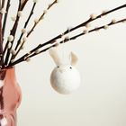 Ein rosafarbener Glasvase mit Weidenkätzchenzweigen und einem hängenden Filzhäschen.