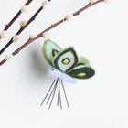 Ein Filzschmetterling in Grün- und Gelbtönen hängt an einem Zweig mit weichen, weißen Knospen.