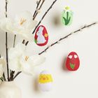 Filzanhänger in Eiform mit Blumen, Hase und Küken, hängend an Zweigen mit weißen Blüten in einer Vase.