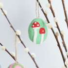 Filz-Osterei mit zwei roten Pilzen auf grünem Hintergrund, hängend an einem Zweig mit flauschigen Knospen.