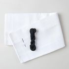 Keine erkennbaren Texte. Zwei weiße Stoffstücke, schwarze Garnrolle und zwei Nadeln darauf.