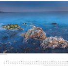 Mai-Kalender mit Strandfoto. Felsen im blauen Wasser, ruhiger Horizont, felsige Küste und sanfte Atmosphäre.