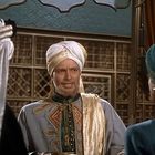 Drei Menschen in orientalischer Kleidung in einem prunkvollen Raum; einer trägt einen Turban und spricht zu den anderen.