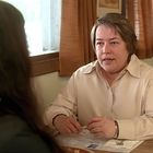 Ich kann es nicht genau sagen. Eine Person im hellen Hemd sitzt am Tisch einer Café-Kabine und spricht mit jemandem.