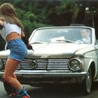 Eine Frau auf Rollschuhen fährt vor einem alten Cabrio, in dem ein Mann sitzt.