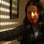 Keine Texte erkennbar. Eine Person mit blutigen Lippen streckt eine Hand aus, im Hintergrund fallen Lichtpunkte auf die Wand.