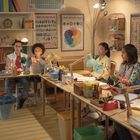 "School and Family Charts." Ein Lehrer spricht zu fünf Schülern an Schreibtischen in einem Klassenzimmer voller Bücher und Poster.