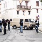 Schild mit "20" und "GAZTAÑO AUZOA". Männer in schwarzer Kleidung, teilweise maskiert, zielen mit Waffen. Transporter.