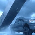 Ein Nissan-Pickup fährt vor einem stürmischen Himmel; ein umgestürzter Truck im Hintergrund.