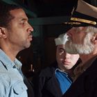 Ein Soldat und ein älterer Mann in Uniform stehen sich ernsthaft gegenüber, umgeben von anderen in Marinekleidung.