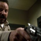 Ein Mann in einer Uniform mit einem "Black Creek" Abzeichen zielt mit einer Pistole, Gesichtsausdruck wütend.