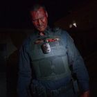 Auf der Uniform steht "BRYCE POLICE". Ein Polizist, blutverschmiert im Gesicht, in einem dunklen, nächtlichen Setting.