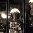 Drei Personen in improvisierter Rüstung aus Technikschrott; einer trägt einen Korb auf dem Kopf, die anderen Helme.