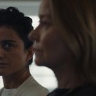 Zwei Frauen im Halbprofil. Die Frau links hat dunkles, die rechts blondes Haar. Beide sehen ernst aus, im Hintergrund Fenster.