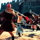 Chinesische Zeichen über einem Tor. Kampf zwischen Kriegern in traditionellen Gewändern mit langen Stangenwaffen.
