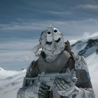 Ein futuristischer Soldat in weißer Rüstung steht vor einer schneebedeckten Berglandschaft und hält eine Waffe.