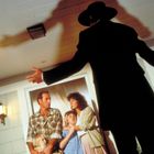 Ein Mann in schwarzem Mantel und Hut wirft einen großen Schatten. Eine Familie wirkt erschrocken und hält sich fest.