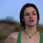 Eine Person trägt ein grünes Top, hat kurzes, nasses Haar und schaut überrascht oder besorgt in die Ferne.