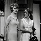 Zwei Frauen in eleganter Kleidung in einem Raum, die eine hält eine Tasche, die andere hat einen ernsten Blick.