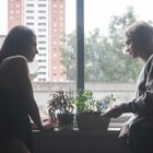 Ich kann dir nicht sagen, wer die Personen sind, aber sie lehnen am Fenster, daneben Pflanzen, mit einem Gebäude im Hintergrund.