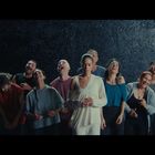 Menschen lachen in einer Gruppe, vor einem dunklen Hintergrund. Eine Person in der Mitte wirkt ernst und nachdenklich.