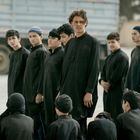 Männer und Jungen tragen schwarze Gewänder und stehen in einer Gruppe im Freien. Im Hintergrund ist ein Lastwagen.