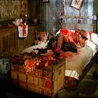 Es gibt keine sichtbaren Texte. Eine blutige Szene in einem dunklen Raum, ein Körper liegt auf einem Bett, umgeben von Chaos.