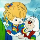 Ein blondes Kind mit Stern im Haar, in Regenbogenklamotten, neben einer flauschigen Kreatur mit roten Knien.