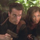 Es gibt keinen Text im Bild. Zwei Personen kauern und halten Waffen, umgeben von Pflanzen im Hintergrund.