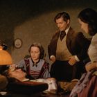 Vier Personen in historischer Kleidung, eine ist krank im Bett, die anderen kümmern sich um ihn. Eine Lampe beleuchtet die Szene.