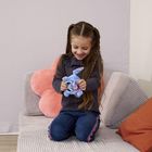 Ein lachendes Mädchen auf einem Sofa mit rosa Kissen, hält ein kleines, blaues Stofftier.