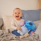Ein fröhliches Kleinkind sitzt lachend auf einem Bett und hält ein blaues Stofftier mit großen Ohren und geschlossenen Augen.
