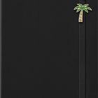 Ein schwarzes Notizbuch mit einem elastischen Verschluss. Darauf sind Pins: ein Surfbrett und eine Palme mit Kristallen.