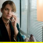 Eine nachdenkliche Frau telefoniert am Fenster, im Hintergrund moderne Büroausstattung.