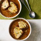 Zwei Schalen mit Zwiebeluppe, garniert mit geschmolzenem Käse auf Brot. Daneben liegen zwei silberne Löffel auf einem grünen Tuch.