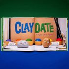 „CLAY DATE: A Playdate with the Claymates“, ein Bild mit Knetfiguren und bunten Kugeln vor einem Korkhintergrund.