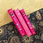 „Sarah Henning, Such a Witch“ steht auf drei rosa Buchrücken, daneben mystische Symbole auf schwarzem Hintergrund.