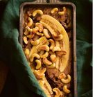 Eine Kastenform enthält Bananascheiben und Cashewnüsse auf einem gebackenen Brot, das auf einem grünen Tuch liegt.