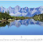 Österreich, Spiegelsee. Kalender mit Bergen im Hintergrund, ruhiger See und grüner Uferlandschaft.