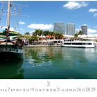 Text: „Miami Bayside“, „HERITAGE OF MIAMI“. Ein Segelschiff im Vordergrund, moderne Gebäude und Palmen im Hintergrund.