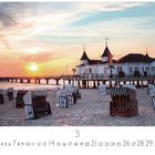 Seebrücke Ahlbeck. Strandkörbe am Sandstrand bei Sonnenuntergang, rechts ein Piergebäude mit Türmen.