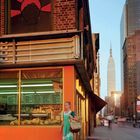 Frau in grünem Kleid vor oranger Hauswand, Schaufenster mit Preistafeln, Skyline mit Empire State Building im Hintergrund.