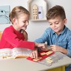 Kinder spielen mit nummerierten Karten. Ein Mädchen im roten Pulli und ein Junge im blauen Hemd lächeln dabei.