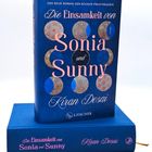 Text: "Die Einsamkeit von Sonia und Sunny", "Kiran Desai", "S. Fischer". Abbildung eines Buchcovers in Blautönen mit Kreismuster.