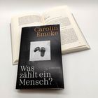"Carolin Emcke: Was zählt ein Mensch?" auf einem Buchcover. Darauf sind Schuhe abgebildet. Ein weiteres Buch ist offen.