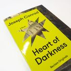 Text: "Joseph Conrad, A Novel, Heart of Darkness, Reclam Originals." Gelbes Buchcover mit gezacktem Stern und Urwaldmotiv.