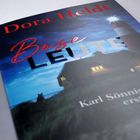 Buchcover mit Texten "Dora Heldt", "Böse Leute", "Karl Sönnigsen". Ein Leuchtturm bei Nacht und ein Haus mit erleuchteten Fenstern.