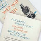 Ein Buchcover zeigt Texte: „EINE GROSSE FREUNDSCHAFT. EIN LAND IN AUFRUHR. EINE SUCHE, DIE ALLES VERÄNDERT.“ Dazu ist ein Foto einer Frau.