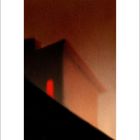 Unschärfe in Rottönen, die an ein abstraktes Gebäude oder Dach erinnert, mit einem auffälligen roten Licht im Vordergrund.