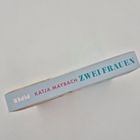 Auf einem Buchrücken steht: "KATJA MAYBACH ZWEI FRAUEN". Er ist in hellblau mit pinkem und teelblauen Text gestaltet.